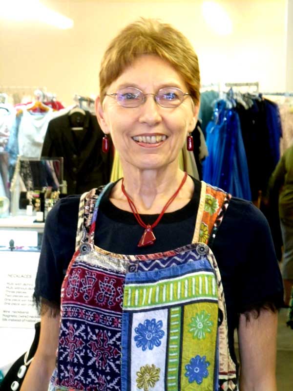 Bonnie relaxes in a dark blue blouse and multicolored overalls, set off by a dark red fused glass pendant and matching earrings.